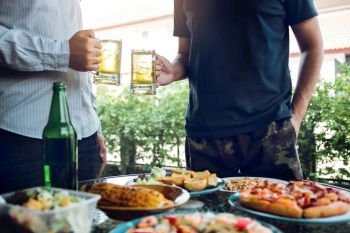 Asian people are socializing outside the house with lots of food on the table and holding a glass of beer inside clinking and enjoy together.
