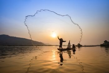 Asia fisherman net using on wooden boat casting net sunset or sunrise in the Mekong river / Silhouette fisherman boat with mountain background people life on countryside 