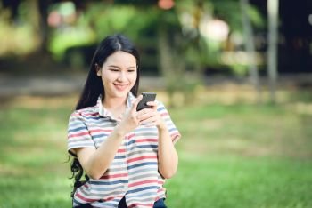 Beautiful asian woman happy and smiling / Young girls student woman playing using smartphone in garden park outdoors 
