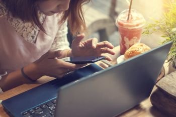 woman using smartphone in coffee shop with laptop