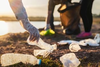 people volunteer keeping garbage plastic bottle into black bag at park river in sunset
