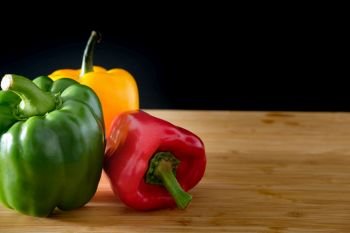 Three bell peppers on a wooden and black background, Space on the right
