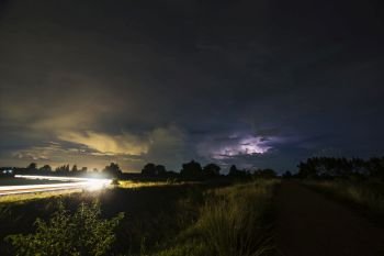 Line of light of car and silhouette of tree,While lightning in the background.