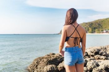 Young asian woman wearing bikini standing facing the sea
