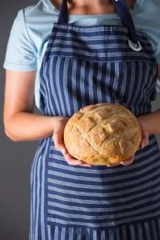 Woman Wearing Apron Holding Freshly Baked Loaf Of Bread