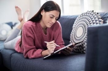 Young Woman Relaxing On Sofa At Home Writing In Journal