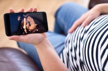 Detail Of Pregnant Woman Looking At 3D Image Of Baby On Mobile Phone