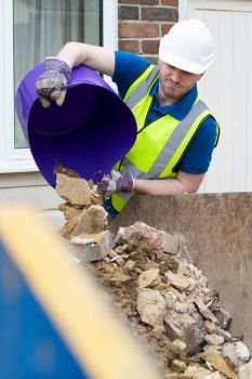 Construction Worker Emptying Building Waste Into Skip Outside Renovated House