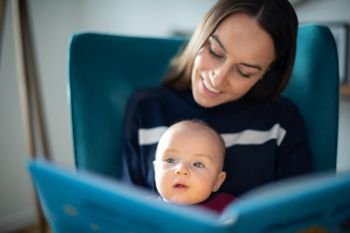 Baby Son Sitting On Mothers Lap Reading Story Book Together