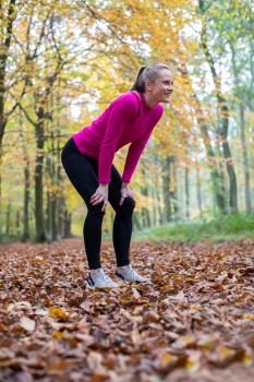 Side View Of Woman On Early Morning Autumn Run Through Woodland Resting After Exercise