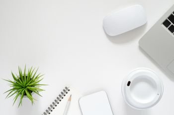 Modern workplace with laptop computer, wireless mouse, coffee cup, smartphone,  notebook, pencil and Tillandsia air plant on white background. Top view, flat lay concept.