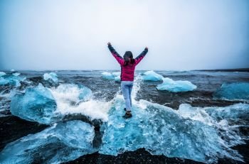 Young woman traveler travel to Diamond Beach in Iceland. Frozen ice on black sand beach known flows from Jokulsarlon beautiful Glacial Lagoon in Vatnajokull National Park, southeast Iceland, Europe.