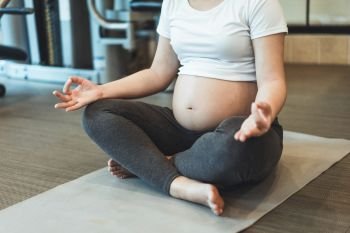 Active pregnant woman exercise in fitness center at yoga room. The young expecting mother holding baby in pregnant belly. Maternity prenatal care and woman pregnancy concept.