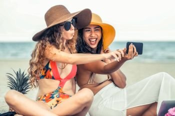 Happy women in bikinis taking selfie photograph from mobile phone together on tropical sand beach in summer vacation. Travel lifestyle.. Happy women taking photo on sand beach in summer.