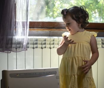 Little girl in a dusty room. Air purifier and coughing kid. Dust in the air. Allergy concept.