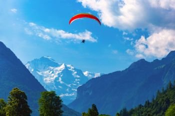A paraglider flying above Interlaken, important tourist center in the Bernese Highlands, Switzerland. The Jungfrau is visible in the background. Paraglider in Interlaken, Switzerland