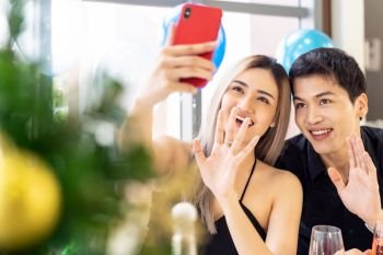 Young asian adult couple make selfie photographing for celebrateing New Year and Christmas holiday together in living room of big apartment in big city.