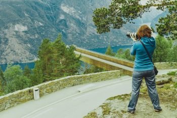 Tourism vacation and travel. Woman tourist taking photo with camera, enjoying Aurland fjord view from Stegastein viewpoint, Norway Scandinavia.. Tourist taking photo from Stegastein viewpoint Norway