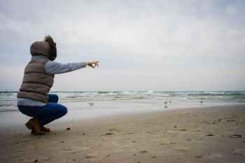 Relaxation and leisure. Woman walking on beach. Female tourist pointing with finger near to water place on nature. Autumn cold season.. Woman walking on beach, autumn cold day