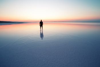 Silhouette of man departing into sunset on smooth water of lake. The concept of privacy and harmony. Silhouette of man departing into sunset on smooth water of lake