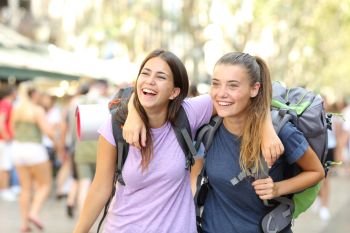 Front view portrait of two happy backpackers laughing enjoying vacation in a city street