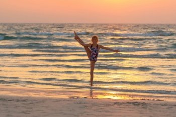 Cute teen girl doing gymnastics on the beach over sunset sky background. Active sportive summer holidays. Healthy childhood.. Teen girl doing gymnastics on the beach