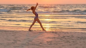 Pretty teen girl doing sport exercise on the beach over sunset sky background. Active sportive summer camp. Dancing near the sea. Healthy childhood.. Teen girl doing exercise on the beach