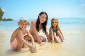 Young mother with two happy kids making a sand castle on the beach. Happy family spending summer vacation on the beach resort. People traveling.. Happy family playing on the beach