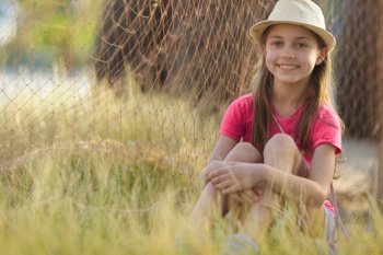 Cute little girl spending summer holidays in countryside. Sitting on the field near fishermans net. Enjoying time outdoors.. Happy girl having fun outdoors