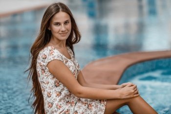 Portrait of a beautiful young female sitting near pool. Spending summer vacation on the beach resort. Happy holidays.. Pretty woman near the pool