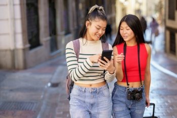 Two young Chinese females passing by guided by the GPS of their smartphone, through the streets of Granada, Spain. Concept of Asian people traveling in Europe.. Asian women travelers pointing away while walking on street