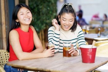 Two young Chinese girls having a drink on the terrace of a typical bar in Granada. Concept of Asian people traveling in Europe.. Two young Chinese girls having a drink on the terrace of a typical bar in Granada.