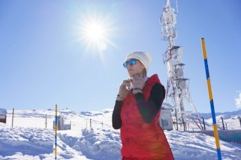 Low angle of focused female in warm clothes and sunglasses putting on headphones while standing in snowy terrain in sunlight. Sportive woman with headphones in winter countryside