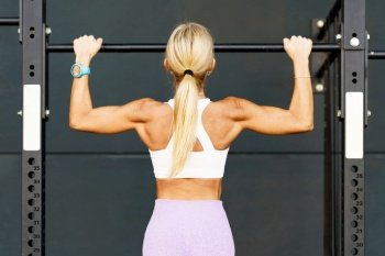 Back view of anonymous female athlete doing pulls up on horizontal bar during workout in gym. Strong woman doing pull ups on barbell in studio