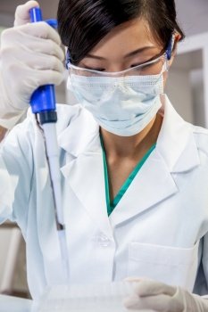 Chinese Asian woman female medical scientist, scientific researcher or doctor using a pipette and cell tray in a medical research lab or laboratory