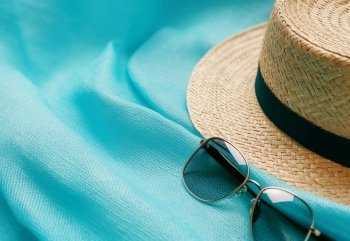 Summer straw hat and sunglasses. Blue summer vacation background. Created with generative Ai technology.