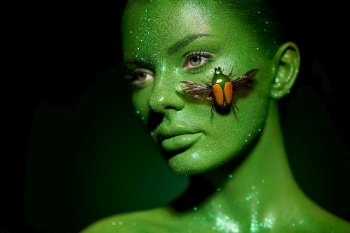 Fashion model woman skin face in bright sparkles with green beetle colorful neon lights, beautiful girl sexy lips. Glowing art green skin make-up. Glitter metallic shine silver green makeup
