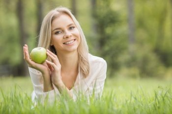 Woman with apple laying on green grass, background with copy space. Woman with apple on grass