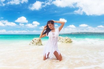 Woman in a white dress is posing on the blue sea beach background. Woman in a white dress on beach