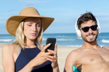 young couple using technology on the beach