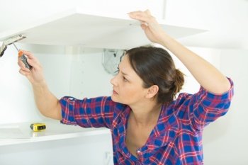 woman tightening hinge on new kitchen cupboard