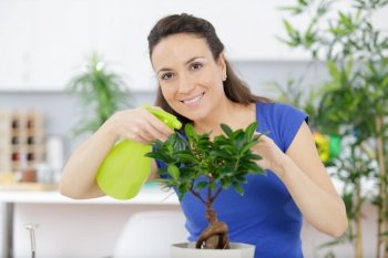 woman sprays water on bonsai tree and smiles