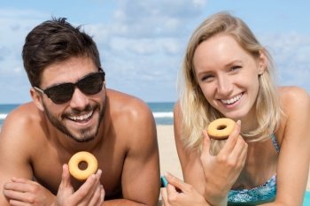 young couple on the beach eating doughnuts