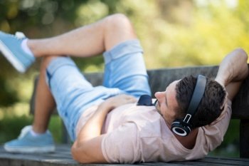 young man with headphones lying on a park bench outdoors