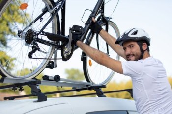 cyclist in helmet instals his bike on the car roof