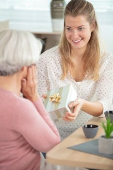 adult daughter giving a gift to her surprised senior mother