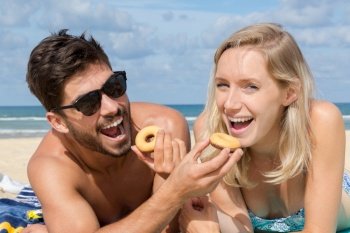 couple swapping donuts on the beach