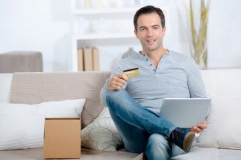 Man holding credit card and laptop, box beside him