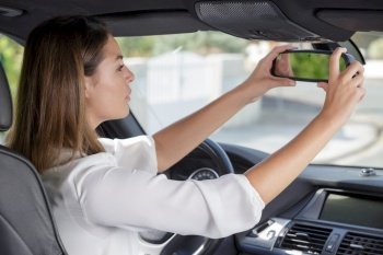 happy young woman driver looking adjusting rear view car mirror