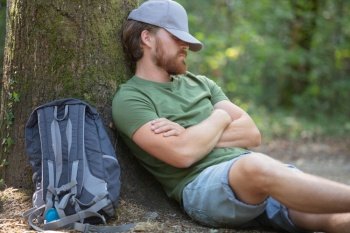 man hiker taking rest sitting at tree in a forest